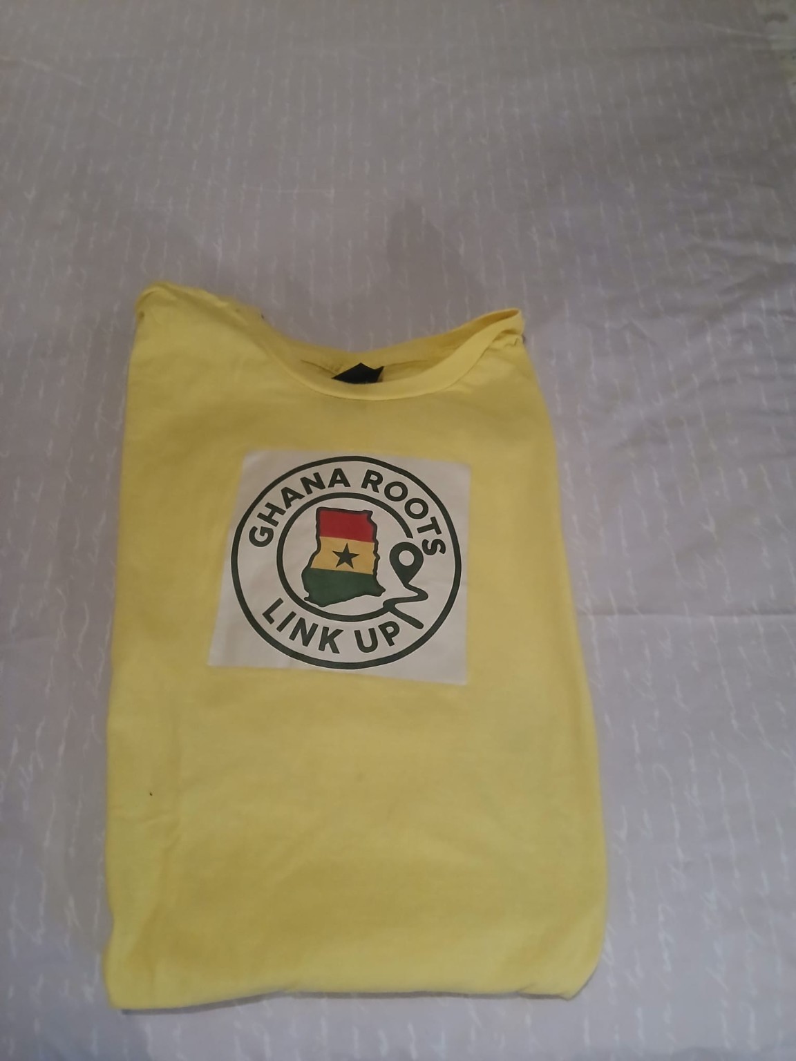 Original photo of the folded yellow Ghana Roots Link Up T-shirt